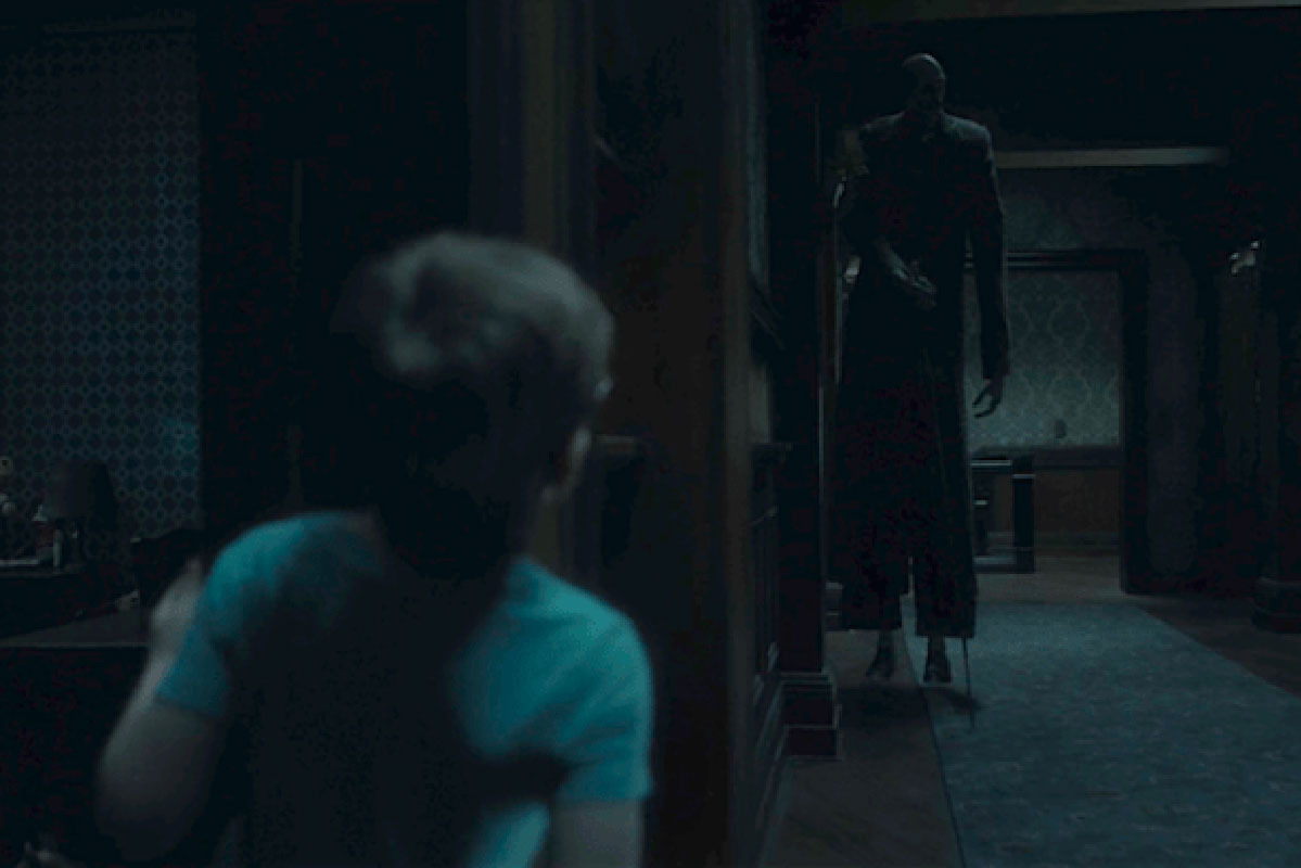 A movie frame showing a boy peeking out of his room and seeing a ghost of a tall man with a cane, stopped next door.